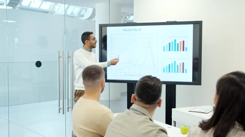 Homem apresentando gráficos em tela grande para plateia em sala corporativa