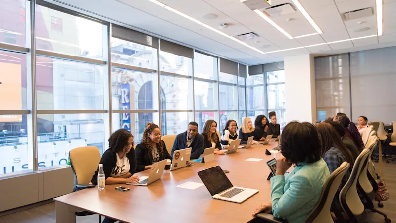 Grupo reunido em mesa de madeira com notebooks em sala de reunião