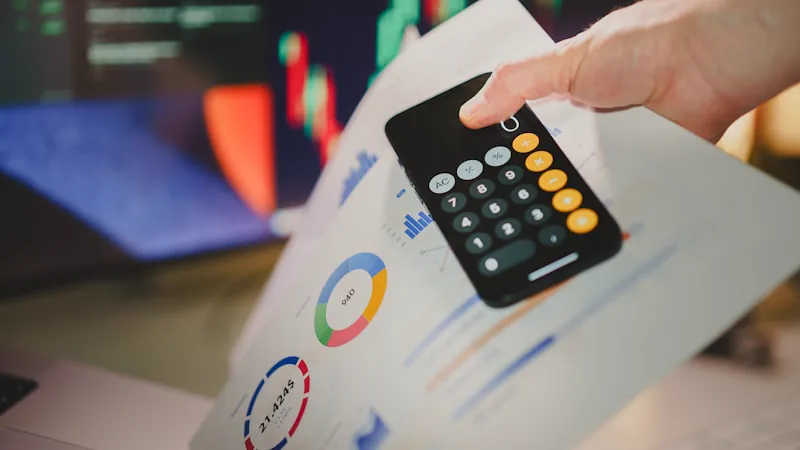 Mão com calculadora sobre planilha impressa com valores