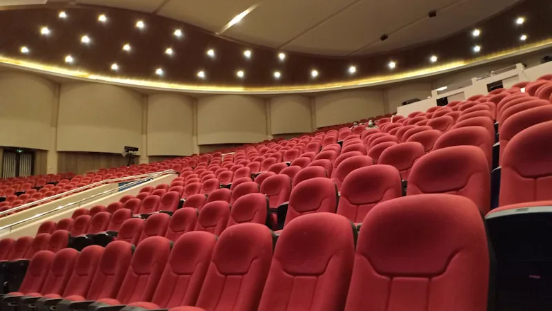 Auditorio amplo com fileiras de poltronas vermelhas vazias