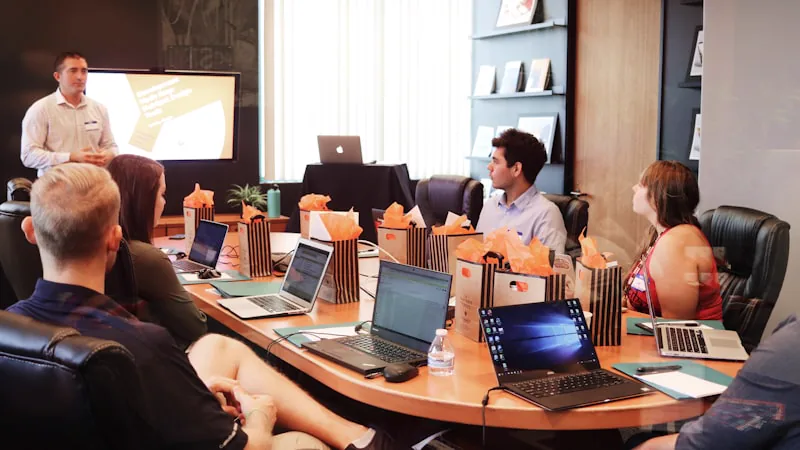 Instrutor apresentando para equipe sentada a mesa com notebooks em treinamento